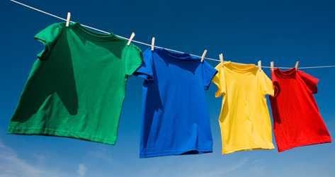 Grupo de 4 camisetas com cores primárias extendidas para secar no varal com fundo de céu azul